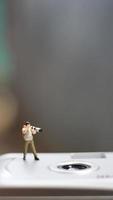 a miniature figure taking picture with a camera against a real camera in the background. photo