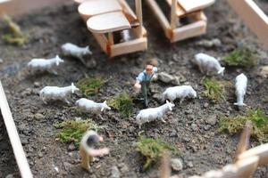 A close up of miniature figure of a goat herder feeding in a wooden cage. Shepherd concept. photo