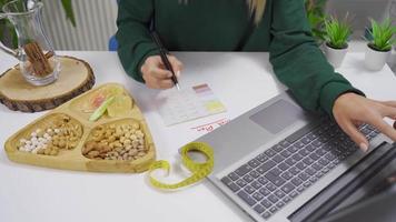 le femme est en train de préparer une régime liste par à la recherche à le l'Internet à maison. là sont des noisettes sur le table de le Jeune femme qui est en train de préparer une nourriture régime programme. video