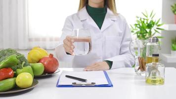 el dietético recomienda comiendo sano y Bebiendo agua. un dietético muestra un vaso de agua a el cámara mientras sentado a su escritorio. video