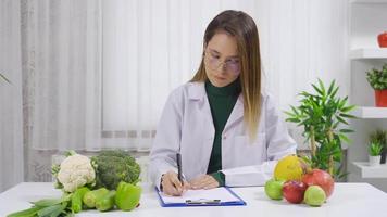 de diëtist bereidt zich voor een eetpatroon lijst voor zijn patiënten met gezond groenten. een vrouw diëtist bereidt zich voor een eetpatroon lijst voor haar patiënten naar hebben een gezond eetpatroon. video