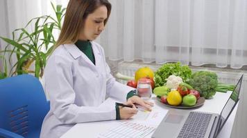 positif diététicien femme travail à table plein de des légumes et des fruits souriant à caméra. diététicien femme satisfait avec sa emploi à la recherche à caméra et souriant. video