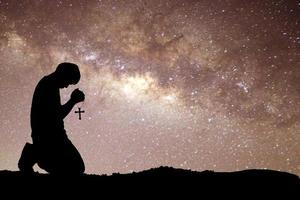 Man silhouette kneeling praying to god hopefully with the beautiful Milky Way photo