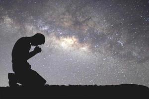 Man silhouette kneeling praying to god hopefully with the beautiful Milky Way photo