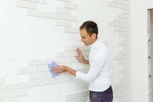 male builder wipes brick tiles on the wall after repair photo