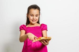 Cute little Indian Asian girl child eating tasty Pizza. Standing isolated over white background. photo
