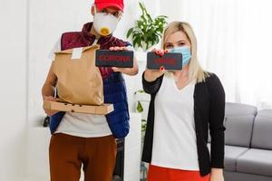 Young woman wearing medical mask receiving parcel from delivery man indoors. Prevention of virus spread photo