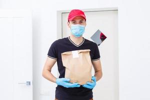 Delivery man holding paper bag with food on white background, food delivery man in protective mask and protective gloves photo