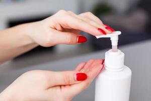 Woman push on dispenser and squeeze out soft soap gel on palm, closeup shot against flat background. Transparent liquid soap used for hand washing photo