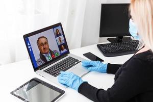 Young woman wearing protective gloves on hands and mask on face working from home or at office work by the laptop video call preventing virus spread epidemic quarantine prevention photo