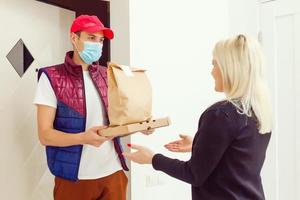 Delivery man holding paper bag with food on white background, food delivery man in protective mask photo