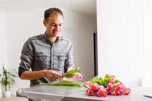 Man florist makes red tulip bouquet and wrapping in pack on wooden table. Flowers photo