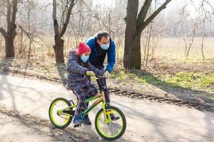 Little girl wearing medical mask prevent flu, pollutions and covid-19 riding bicycle outdoor. photo