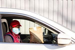 Man in red cap giving fast food order. courier holds paper packet with food. Products delivery from shop or restaurant to home. photo