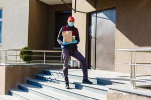 Courier in protective mask and medical gloves delivers takeaway food. Delivery service under quarantine, disease outbreak, coronavirus covid-19 pandemic conditions. photo