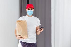 Delivery man holding paper bag with food on white background, food delivery man in protective mask photo