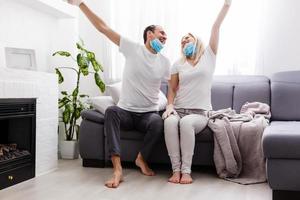 A young couple is sitting at home on self-quarantine. Husband and wife quarantined coronavirus in protective masks. New reality. Normal life in isolation. Read a book together. Italy europe covid-19 photo