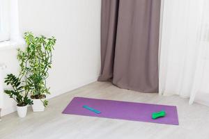 Unrolled yoga mat on wooden floor in modern fitness center or at home with big windows and white brick walls, comfortable space for doing sport exercises, meditating, yoga equipment photo