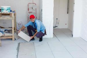 Maestro es instalando piso cerámico loseta en un habitación, prensado abajo y arrasamiento, interior refinamiento de local de un vivo casas foto