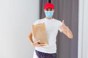 entrega hombre participación papel bolso con comida en blanco fondo, comida entrega hombre en protector máscara foto