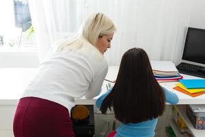 A small girl with her mother are making exercises in copybook at distance home schooling, quarantine photo