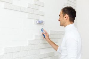 young man paints a brick tile with a roller photo