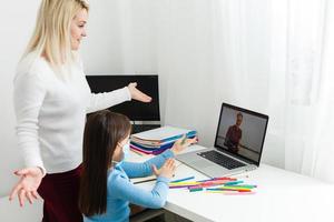 un pequeño niña con su madre son haciendo ejercicios en libro de copiar a distancia hogar enseñanza, cuarentena foto