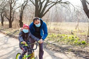 Little asian girl rides bicycle in the park at home and wearing protection mask for protect pm2.5 and Coronavirus Covid-19 Pandemic virus symptoms. photo