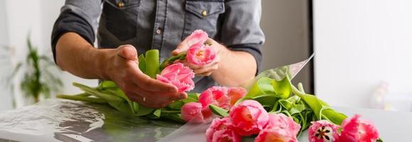 Man florist makes red tulip bouquet and wrapping in pack on wooden table. Flowers photo