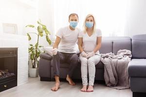 A young couple is sitting at home on self-quarantine. Husband and wife quarantined coronavirus in protective masks. New reality. Normal life in isolation. Read a book together. Italy europe covid-19 photo