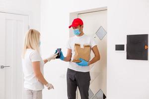 Courier in protective mask delivers parcel, customer in medical gloves receives box. Delivery service under quarantine, disease outbreak, coronavirus covid-19 pandemic conditions. photo