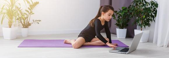 solo niña haciendo yoga ejercicios en línea en ordenador portátil en el piso en el ligero habitación, permanecer hogar seguro mundo. foto