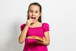 Cute little Indian Asian girl child eating tasty Pizza. Standing isolated over white background. photo