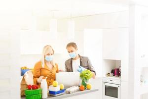 Young Caucasian couple in protective masks doing shoppings at home, quarantine photo