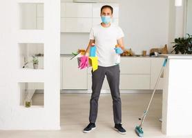 cleaning, health and hygiene concept - indian man wearing protective medical mask for protection from virus disease in gloves with detergent and mop at home photo