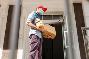 Delivery man holding paper bag with food on white entrance of house background , food delivery man in protective mask photo