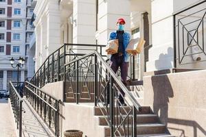 Delivery man holding paper bag with food on white entrance of house background , food delivery man in protective mask photo