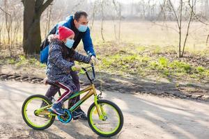 Caucasian father helping daughter ride bicycle wearing protection mask for protect pm2.5 and Coronavirus Covid-19 Pandemic virus symptoms. photo