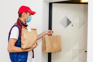 Delivery man holding paper bag with food on white background, food delivery man in protective mask photo