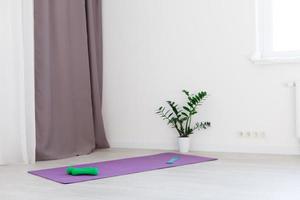 Unrolled yoga mat on wooden floor in modern fitness center or at home with big windows and white brick walls, comfortable space for doing sport exercises, meditating, yoga equipment photo