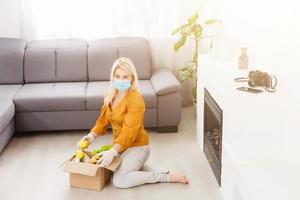 woman wearing medical face mask Disassembles food bags at home in the kitchen. quarantine. health concept. Corona Virus. order of products online. Delivering products to home photo