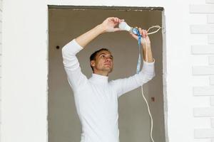 Handsome young builder in a yellow construction helmet is twisting the light bulb in. The man is looking up . photo