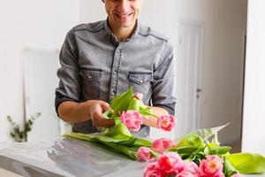 Man florist makes red tulip bouquet and wrapping in pack on wooden table. Flowers photo