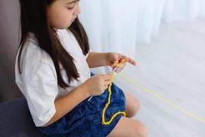 little girl knits crochet. The girl sits on the couch and knits from knitting yarn. Crochet thick threads. Home comfort. photo