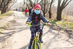 7 7 años antiguo contento pequeño niña niño paseo bicicleta en el parque a hogar y vistiendo proteccion máscara para proteger pm2.5 y coronavirus covid-19 pandemia virus sintomas.deporte ejercicio para salud. foto
