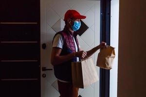 entrega hombre participación papel bolso con comida en blanco fondo, comida entrega hombre en protector máscara foto