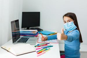 Digital technology education concept. little girl in a protective mask at distance home schooling, quarantine photo