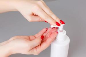 Woman push on dispenser and squeeze out soft soap gel on palm, closeup shot against flat background. Transparent liquid soap used for hand washing photo