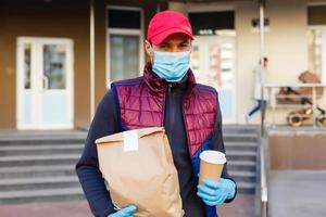 Delivery man holding paper bag with food on white entrance of house background , food delivery man in protective mask photo