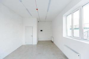 Light room with window and heating battery. Wall is of white plaster, has several outlets. Professional installation of electrical sockets, wires and switches. Connecting the light in flat or office photo